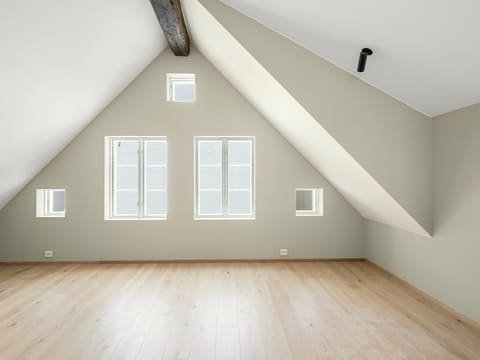 Combles aménagés : pièce lumineuse sous rampants, poutre apparente, murs clairs et parquet en chêne