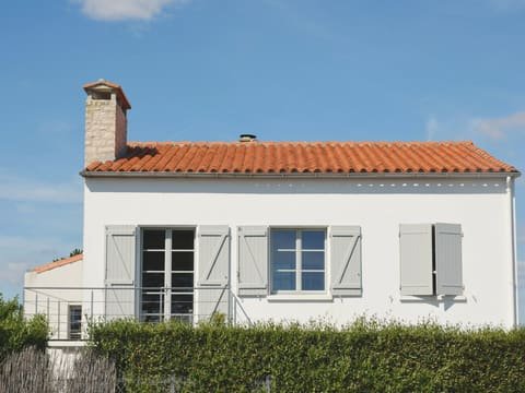 Maison à la façade blanche fraîchement repeinte, volets gris-bleu et toiture en tuiles